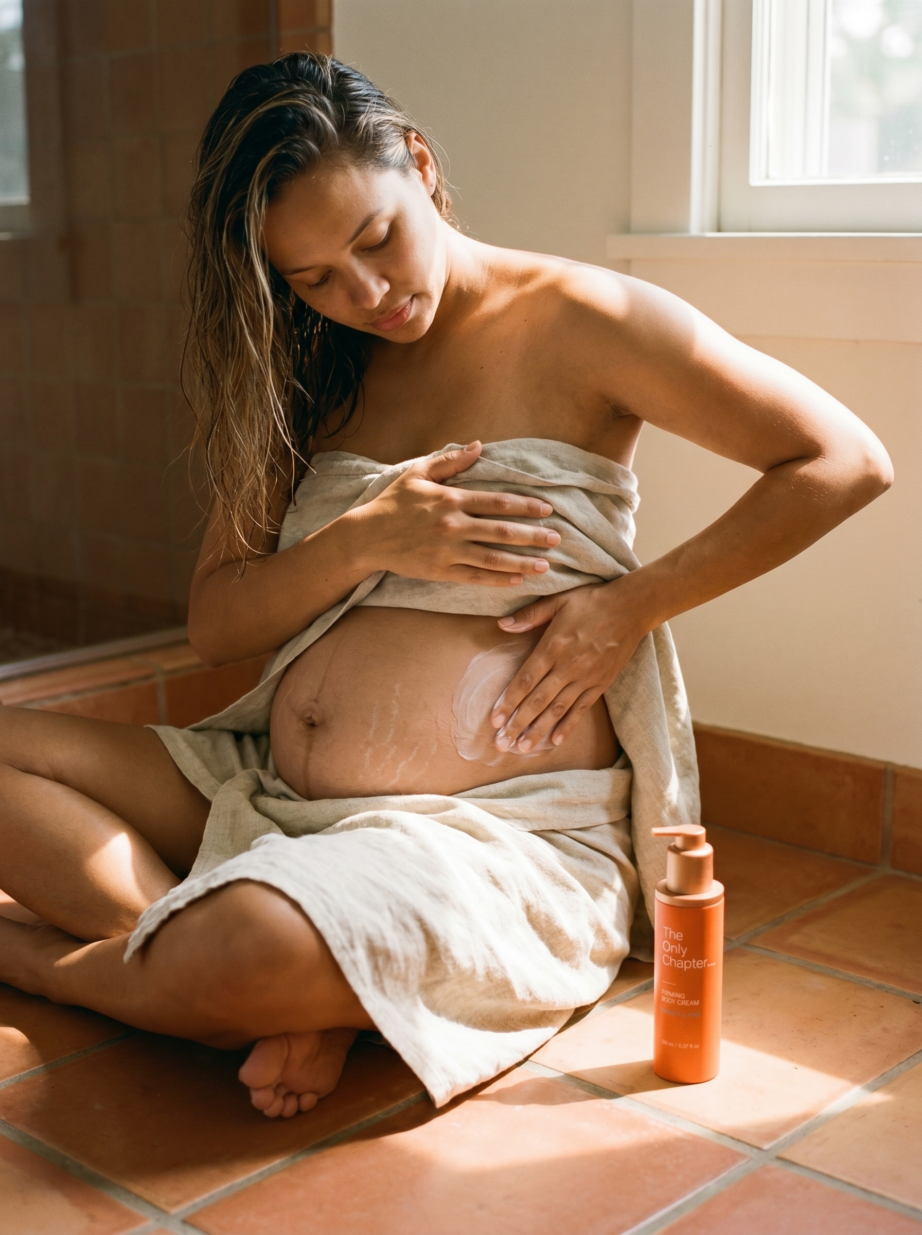 A pregnant woman in a linen towel applying Firming Body Cream