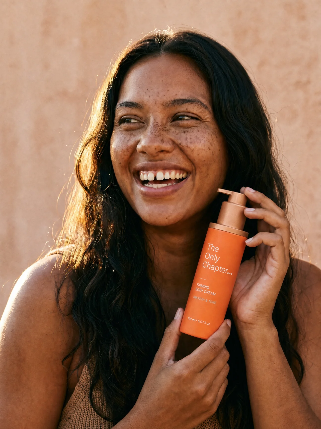 A young woman smiling holding the Firming Body Cream bottle in golden light